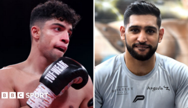 Abdul Khan (left) holds up his hand is wearing a black boxing glove and Amir Khan (right) is wearing a grey t-shirt
