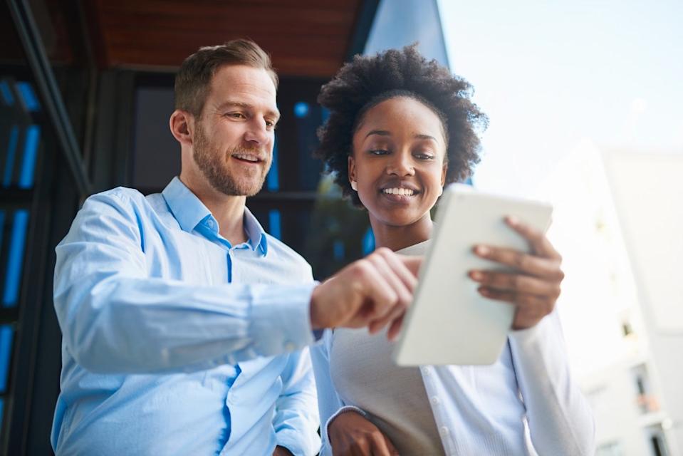 Two investors look at something on a notepad while standing outdoors.