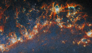 A large, long portion of one of the spiral arms in galaxy M51. Red-orange, clumpy filaments of gas and dust that stretch in a chain from left to right comprise the arm. Shining cyan bubbles light up parts of the gas clouds from within, and gaps expose bright star clusters in these bubbles as glowing white dots. The whole image is dotted with small stars. A faint blue glow around the arm colors the otherwise dark background.