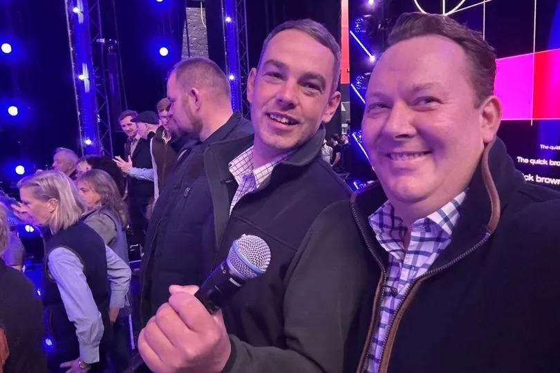 Two men smiling, one holding a microphone