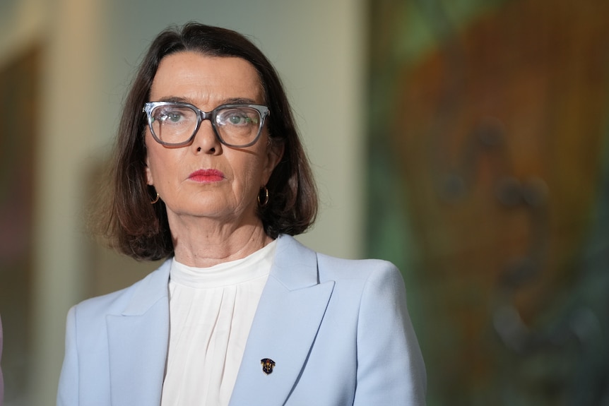 A woman in a powder blue-coloured suit looks sternly toward the camera.