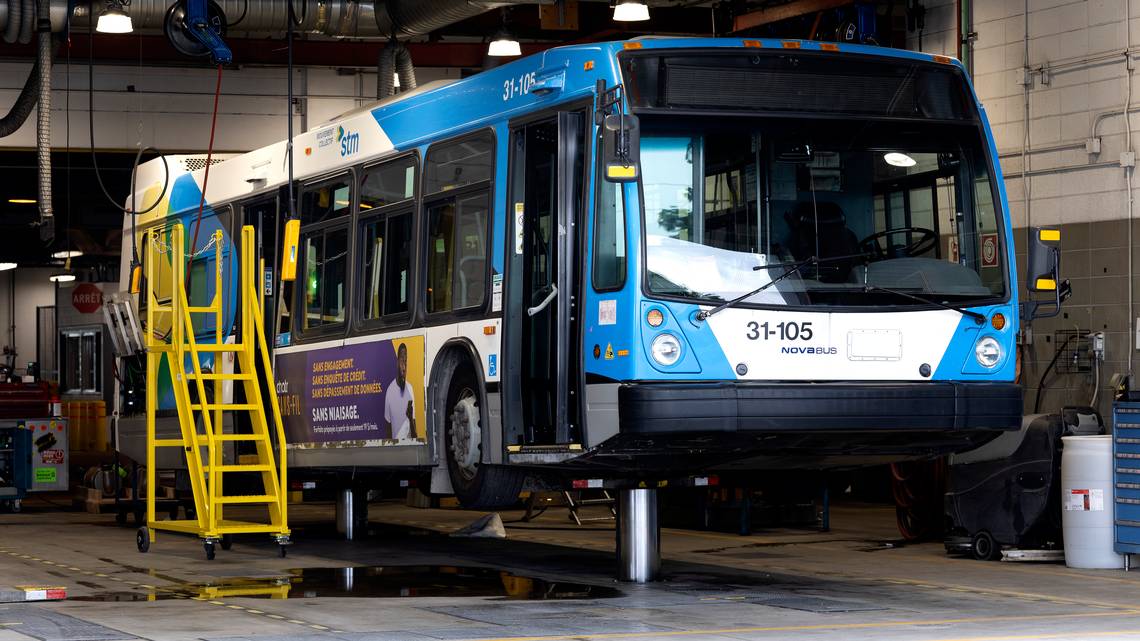An STM bus sits on a hoist in a garage.