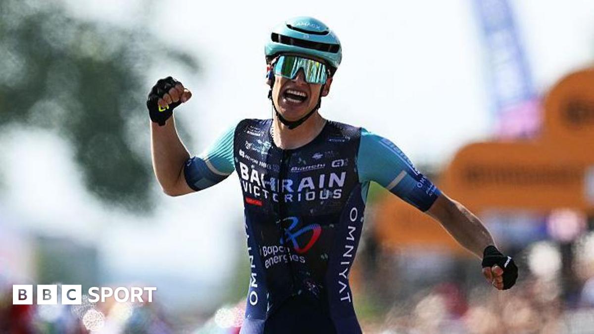 Alec Segaert celebrates by appearing to punch the air, while wearing Bahrain-Victorious cycling outfit, a helmet and sunglasses