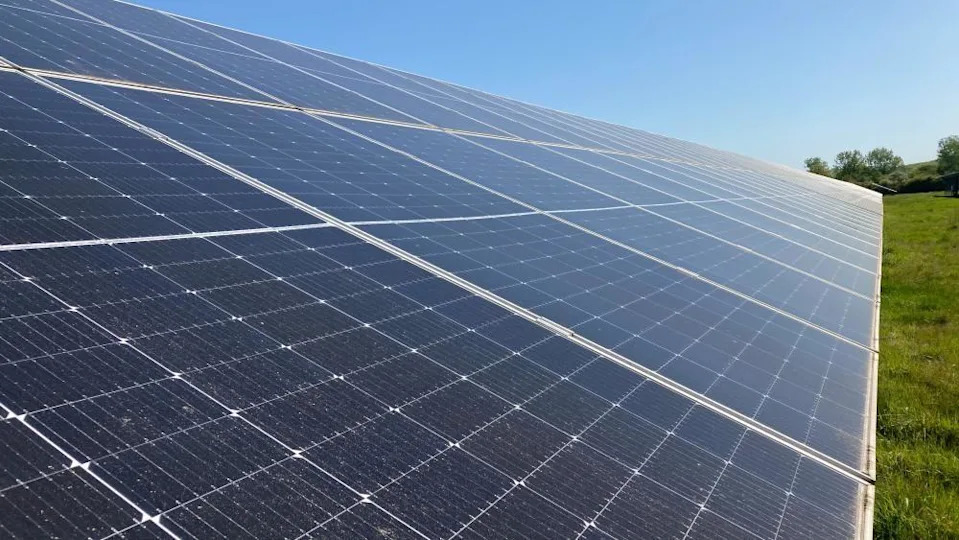 A long row of solar panels. The sky above is blue.
