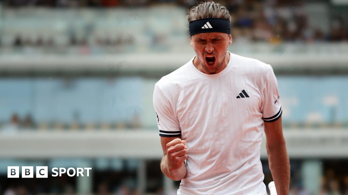 Alexander Zverev, wearing a white t-shirt and black headband, roars with his mouth wide open and clenches his right fist in celebration