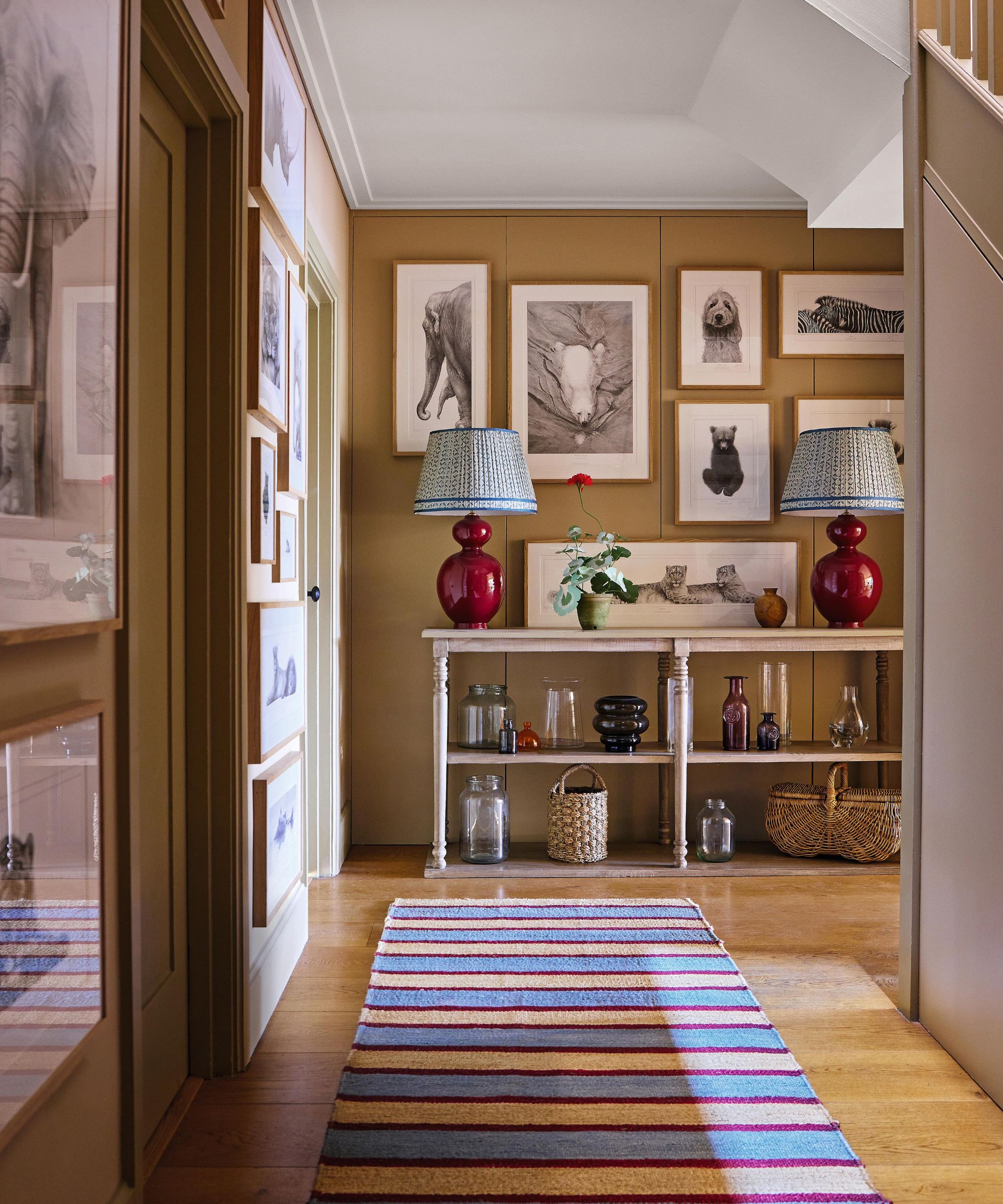 a basement hallway with eclectic gallery wall, console table with two red lamps and a striped runner rug