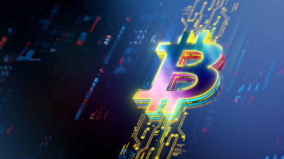 A Bitcoin symbol rests on a screen displaying computer code and illuminated circuit boards.