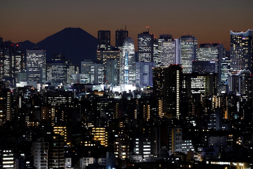 The large conical silhouette of Mount Fuji behind skyscrapers lit after sunset.