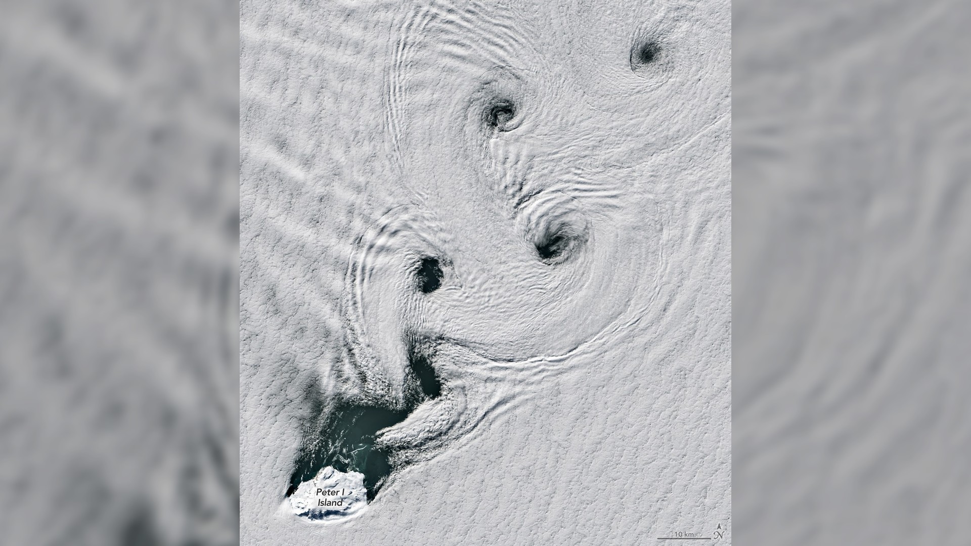 A white, snowy artic landscape has large swirling patterns with small holes or gaps at their center with what appears to be dark water underneath.