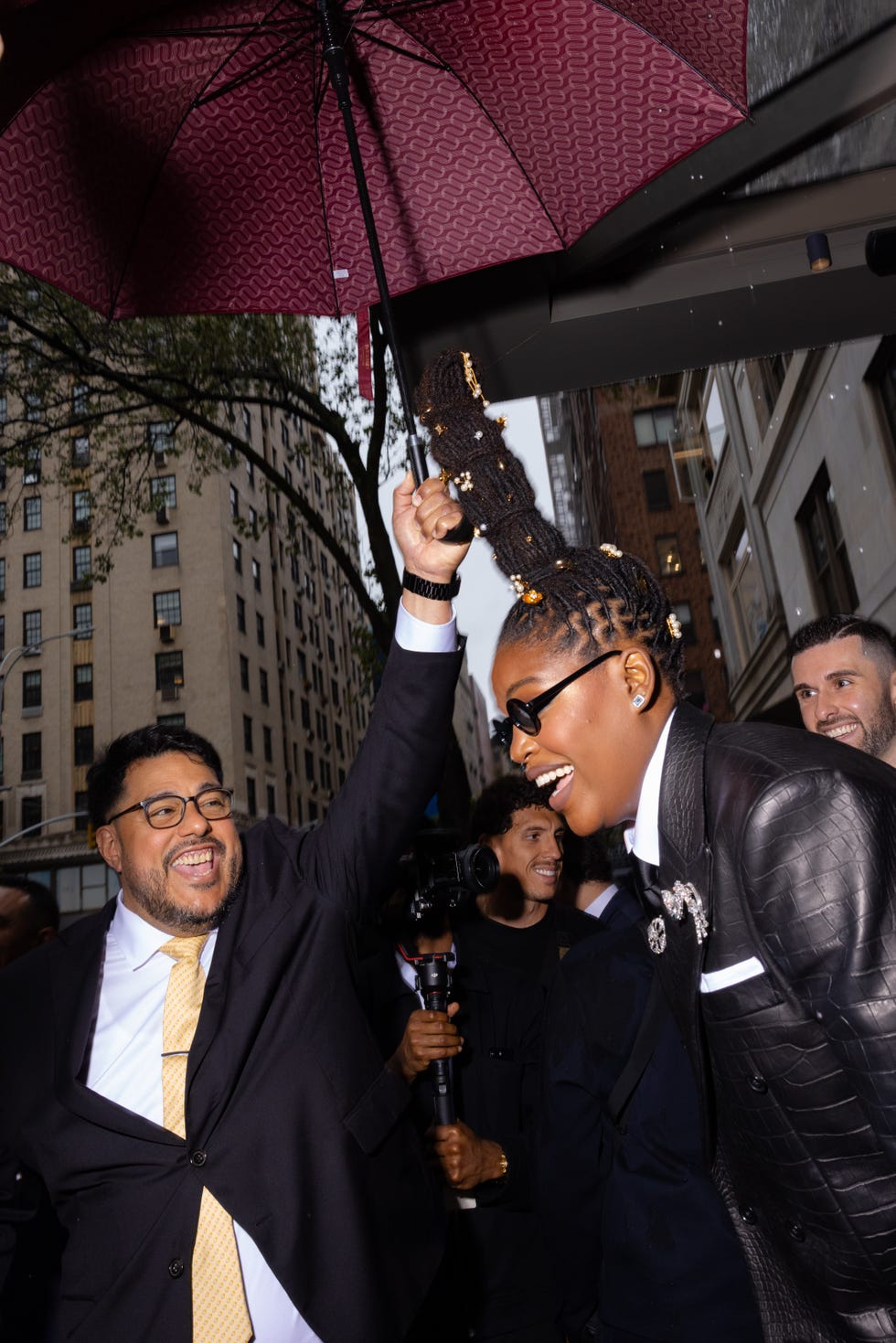 A crowd outside with an individual holding an umbrella and another person styled with unique hair.