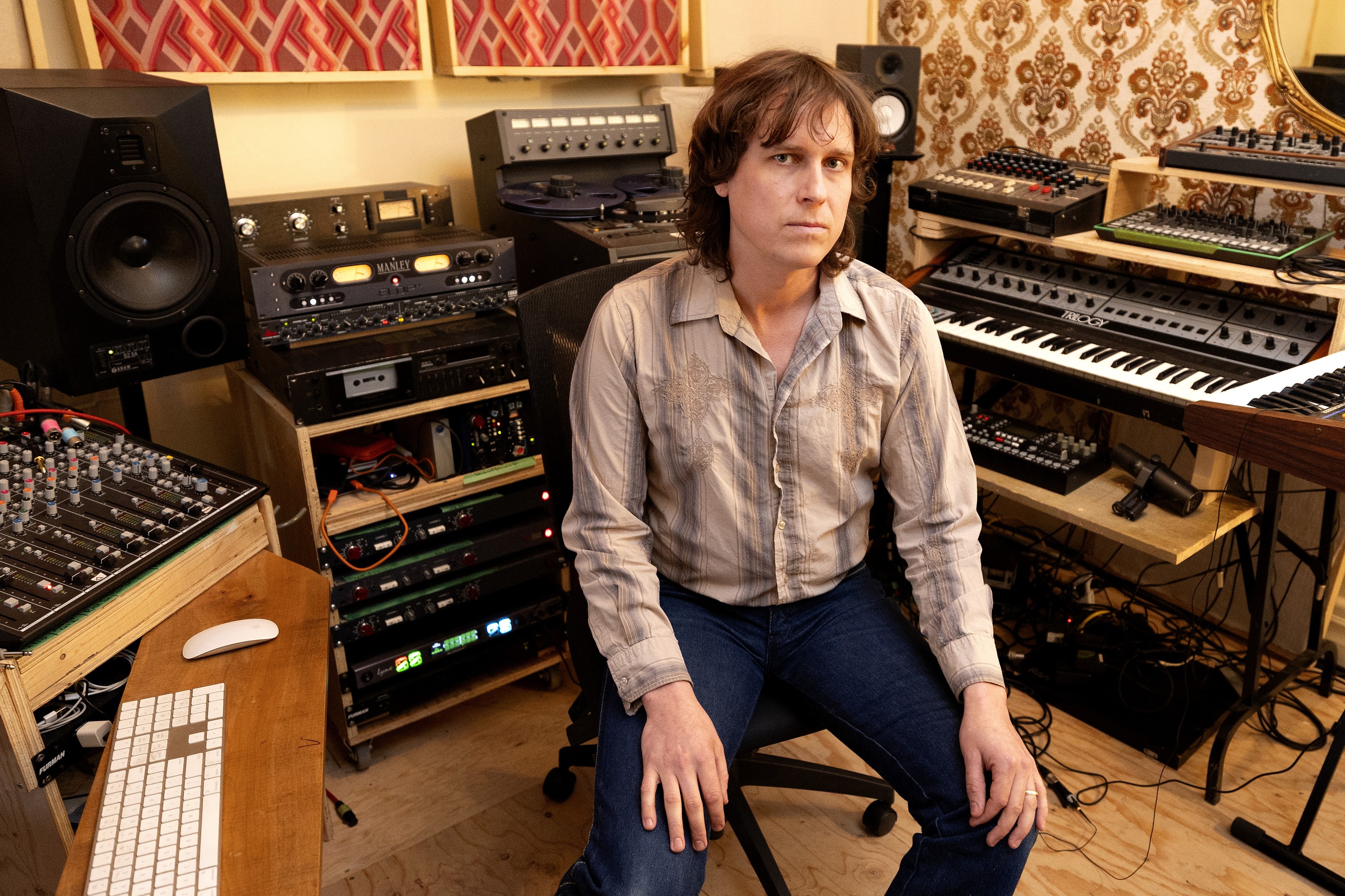 Man sittin gin recoding studio surrounded by music equipment 