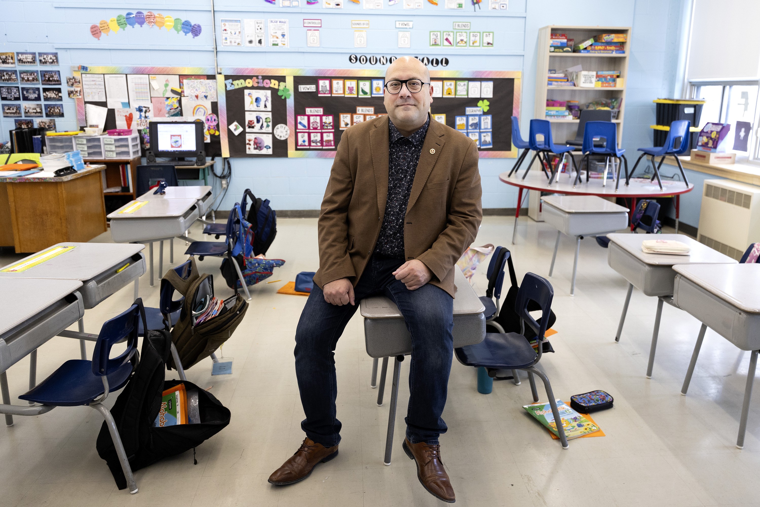 English Montreal School Board chair Joe Ortona sits on a small desk in an elementary school classroom.