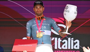 Ganna holds a huge glass and box on the podium, prizes for winning stage 10