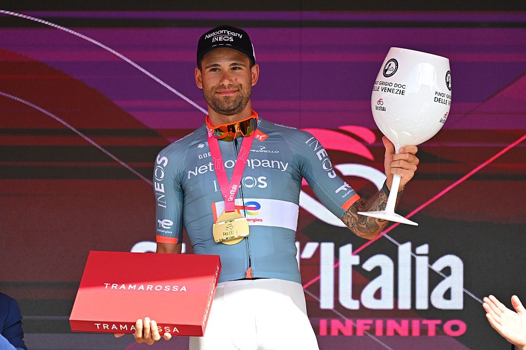 Ganna holds a huge glass and box on the podium, prizes for winning stage 10