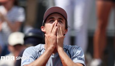 Zachary Svajda, wearing a grey t-shirt and cap, holds his hands to his face in disbelief after winning