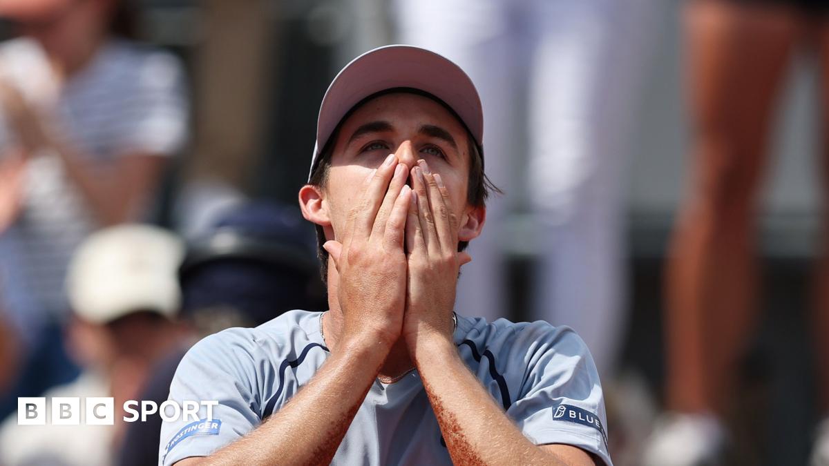 Zachary Svajda, wearing a grey t-shirt and cap, holds his hands to his face in disbelief after winning