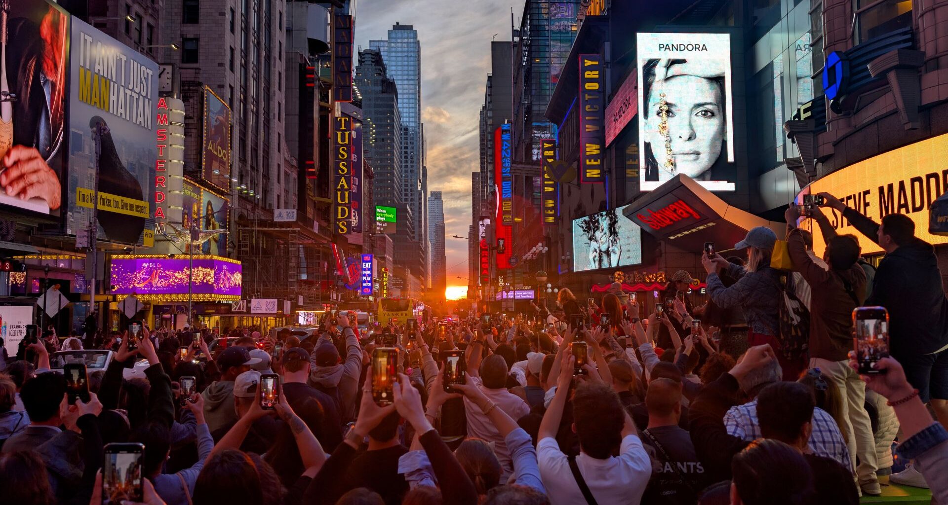 people taking photos of manhattanhenge with the sun setting lining up with the street