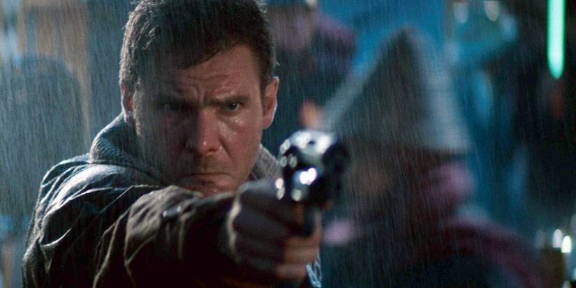 Rick Deckard (Harrison Ford) stands in the rain, scowling, and points a gun toward the camera in Blade Runner (1982)