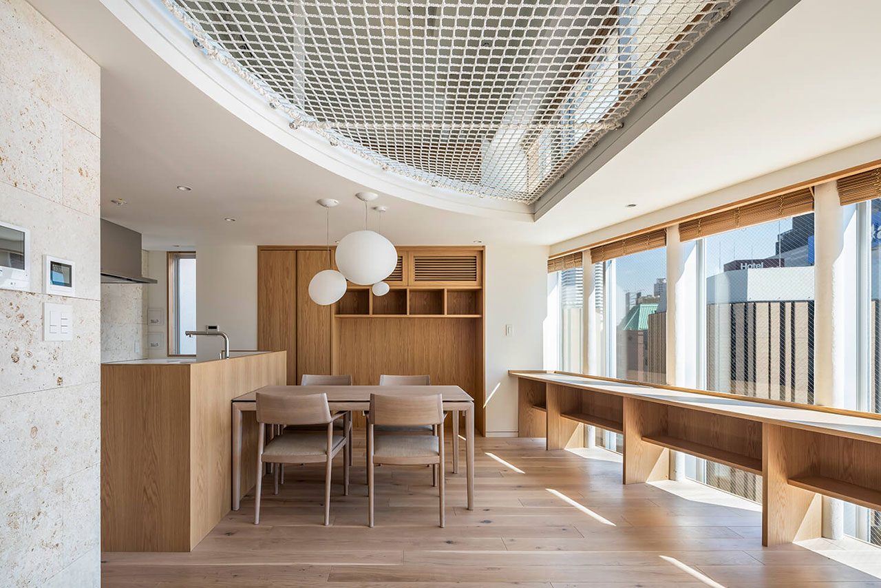 Modern dining and kitchen area with wood finishes, large windows, built-in desk, and an overhead net suspended from the ceiling.