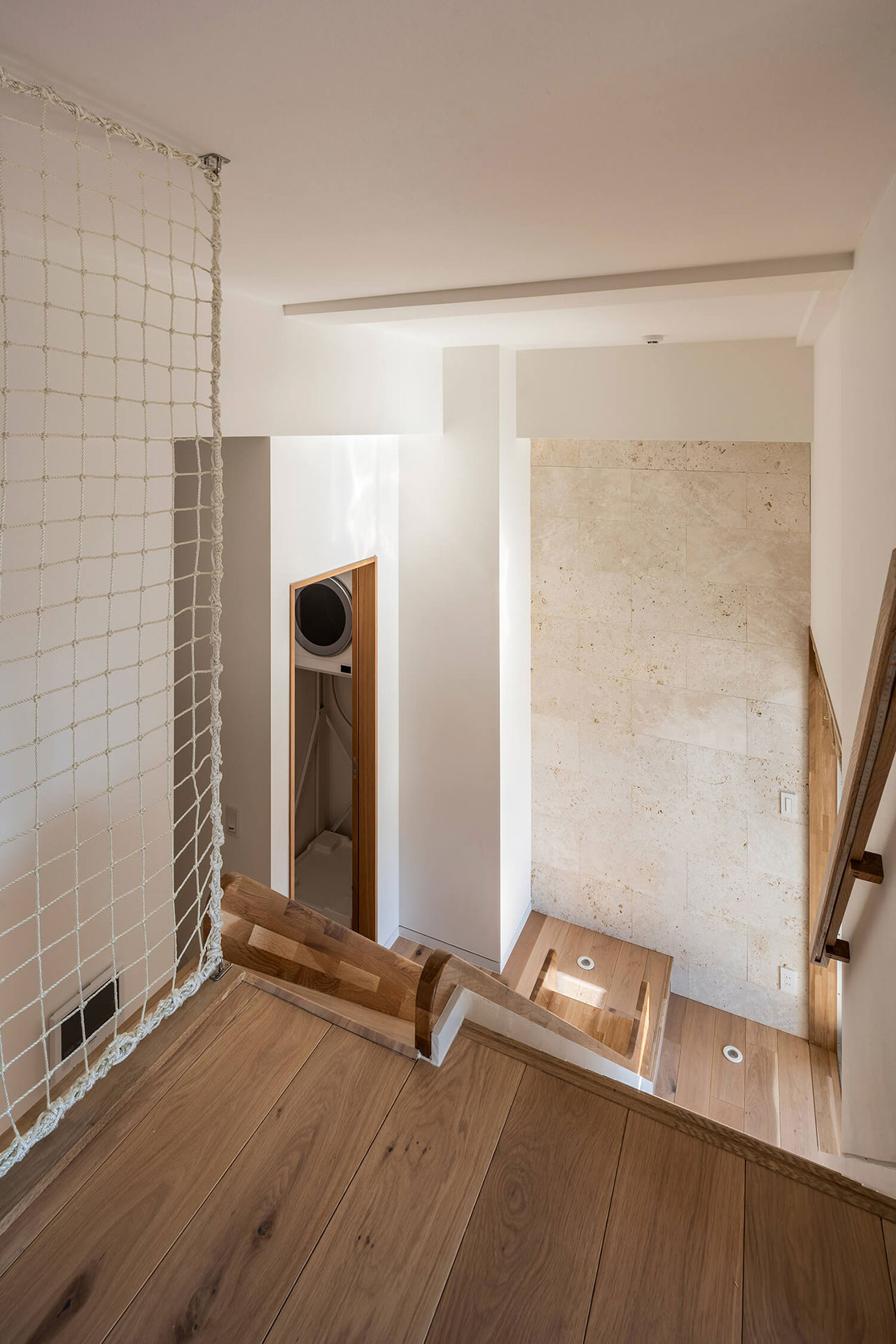 View from a wooden loft area with a safety net, looking down at a modern staircase with beige walls and recessed lighting.
