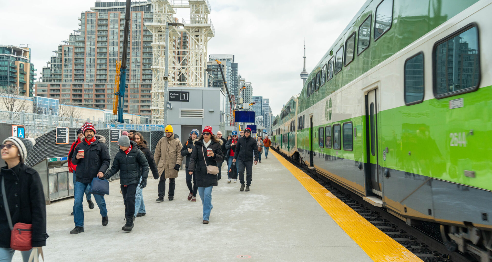 Passengers walking beside a GO train with the CN Tower visible in the background.