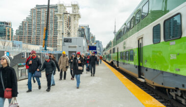 Passengers walking beside a GO train with the CN Tower visible in the background.