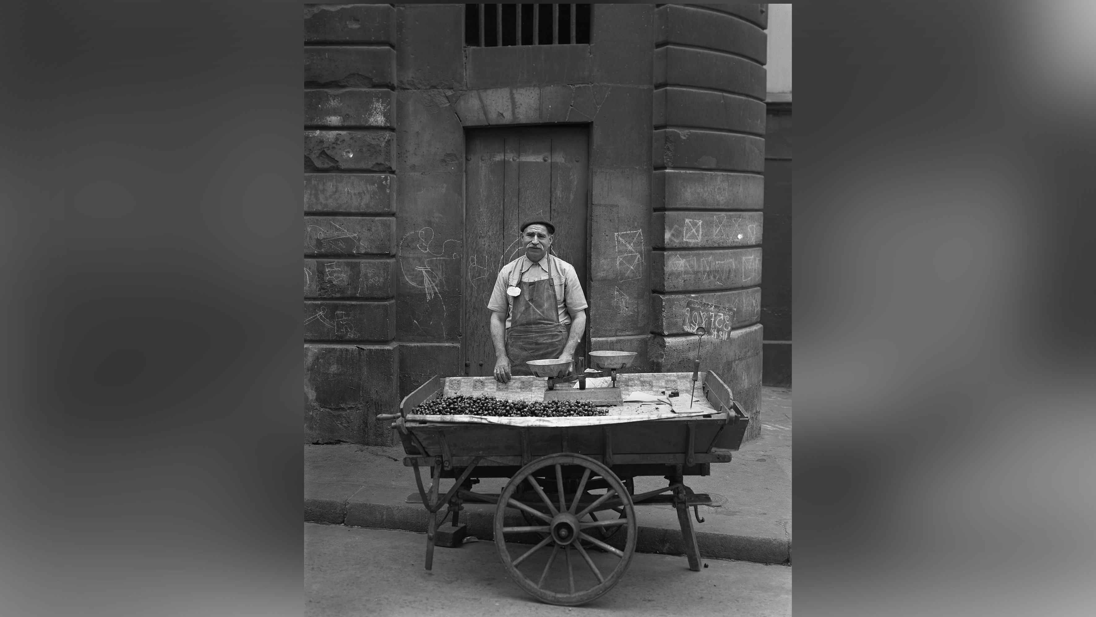 Man stands behind cart selling items in the street.