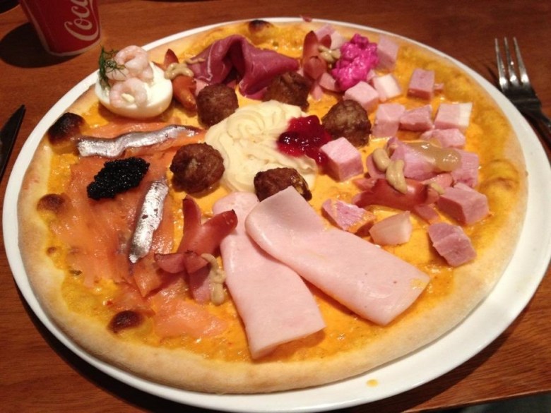 Pizza whose toppings include whole small fish, a devilled egg, and cubed and sliced pieces of deli meats