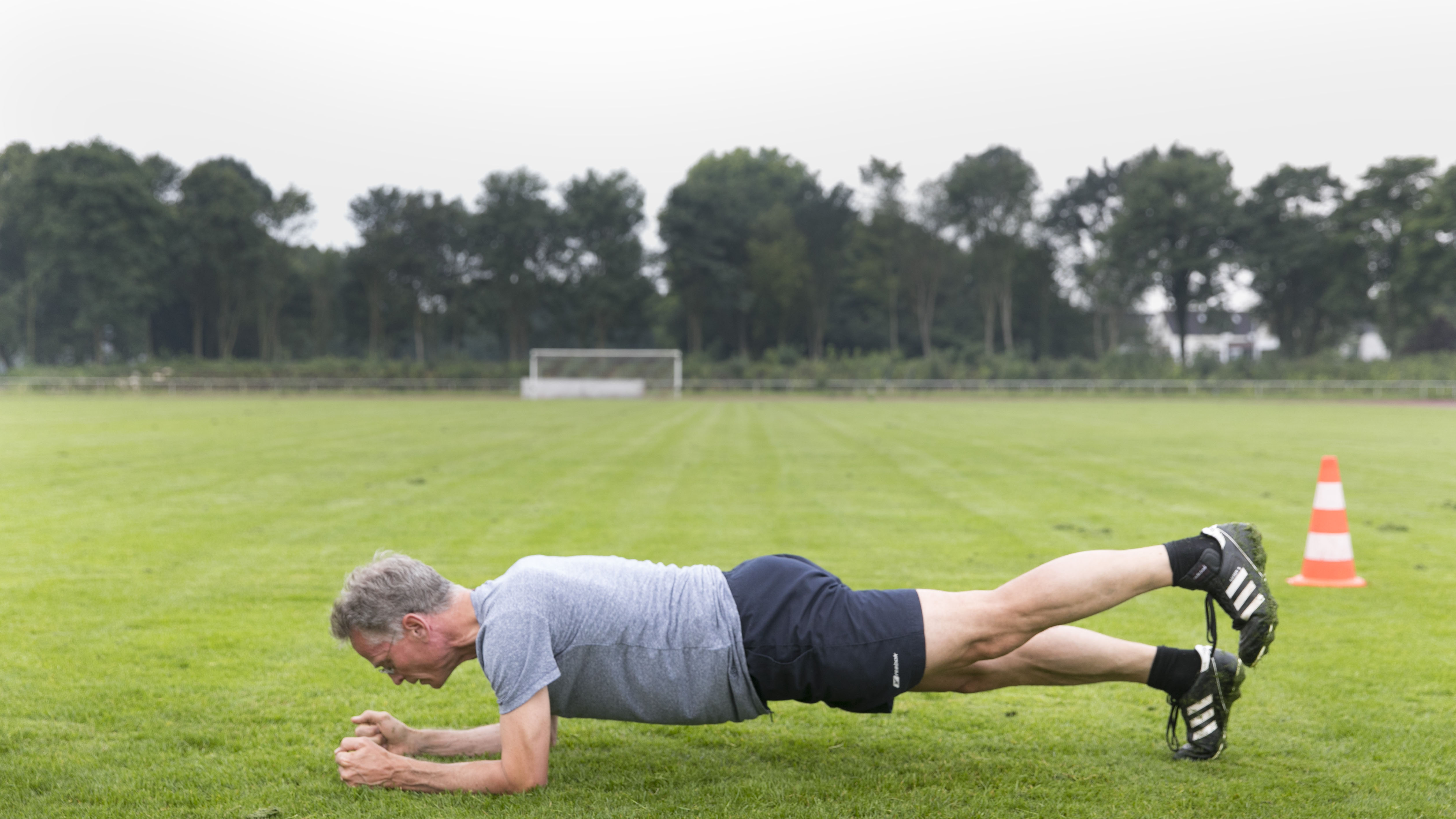 Leisure sports, personal fitness. A man is practicing a forearm stand on a sports field.