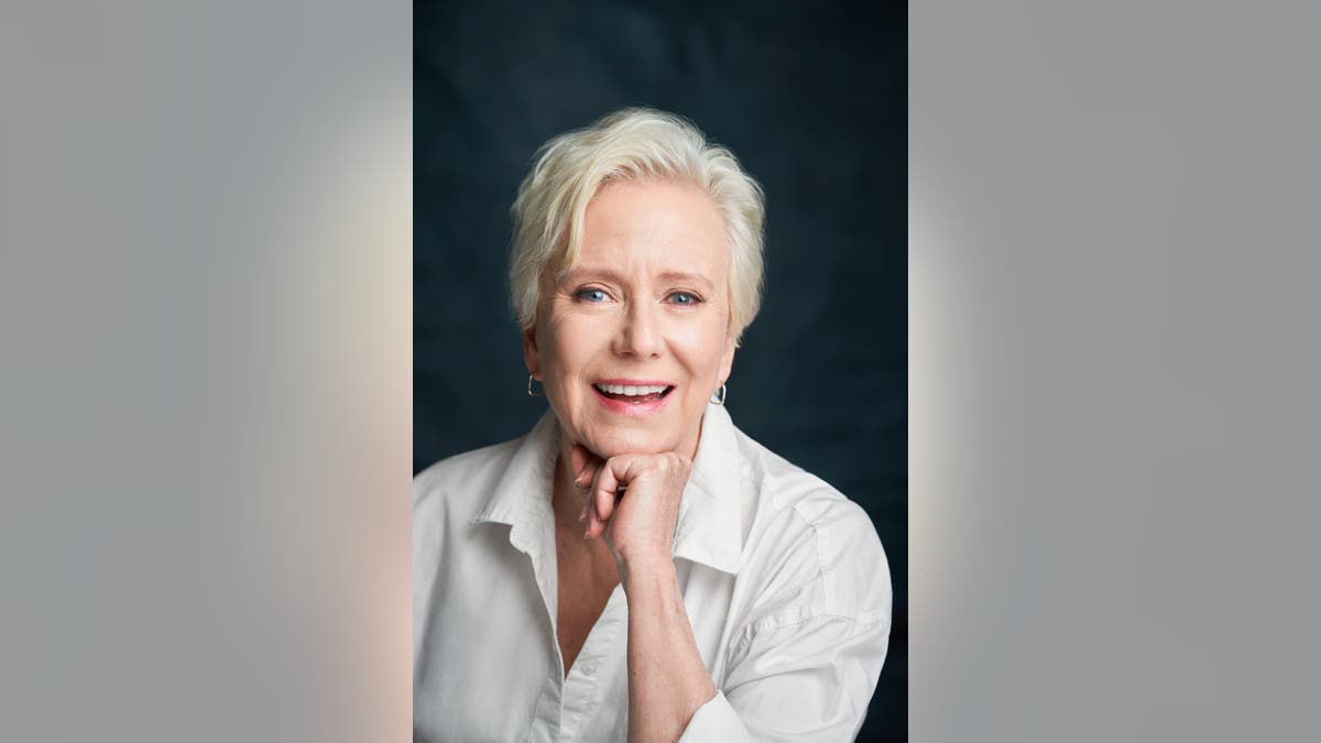 Close-up portrait of Eve Plumb with short light-blonde hair smiling gently.