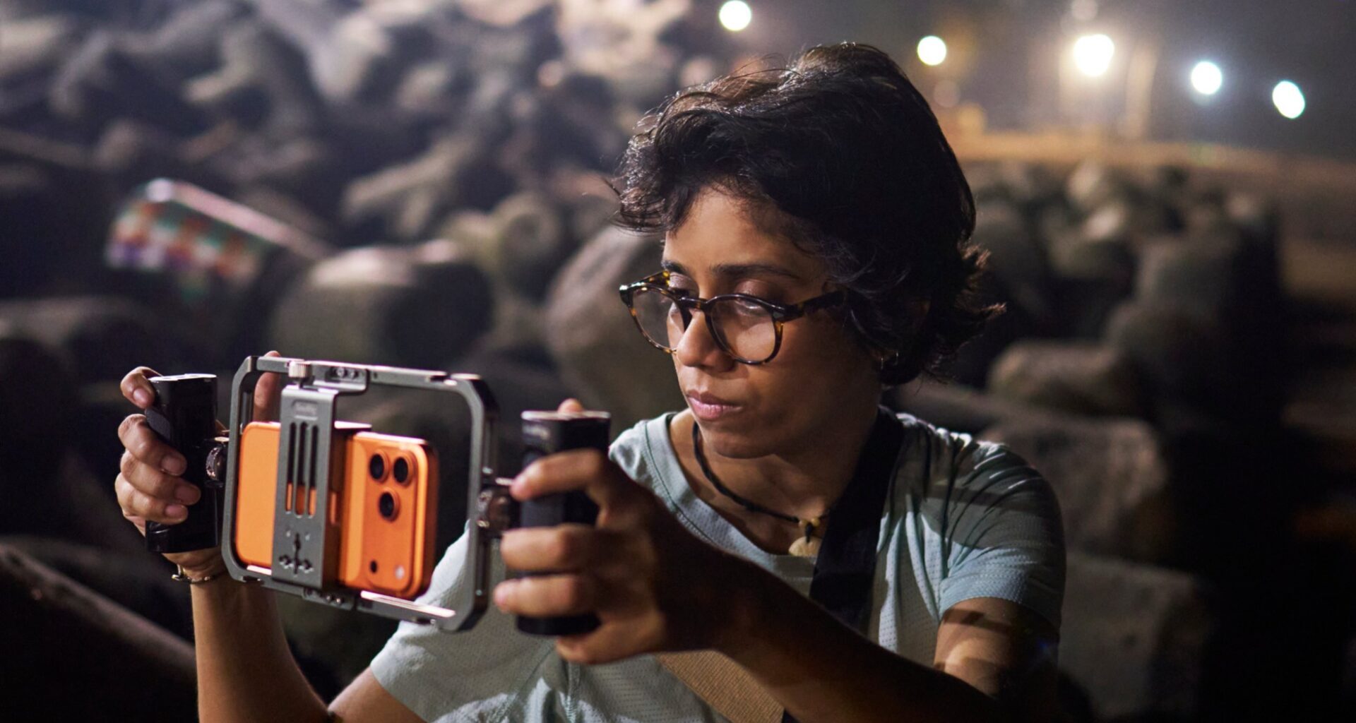 Person wearing glasses uses a handheld camera stabilizer to film outdoors at night.