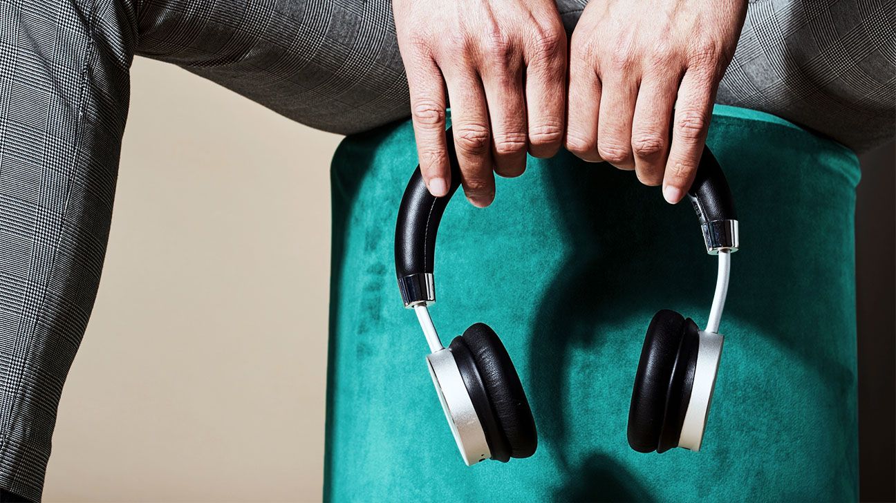 Person holding a pair of headphones against a teal background