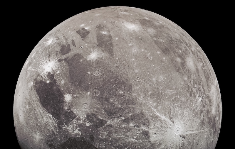 Moon-like gray body with rayed crater and bright and dark patches.