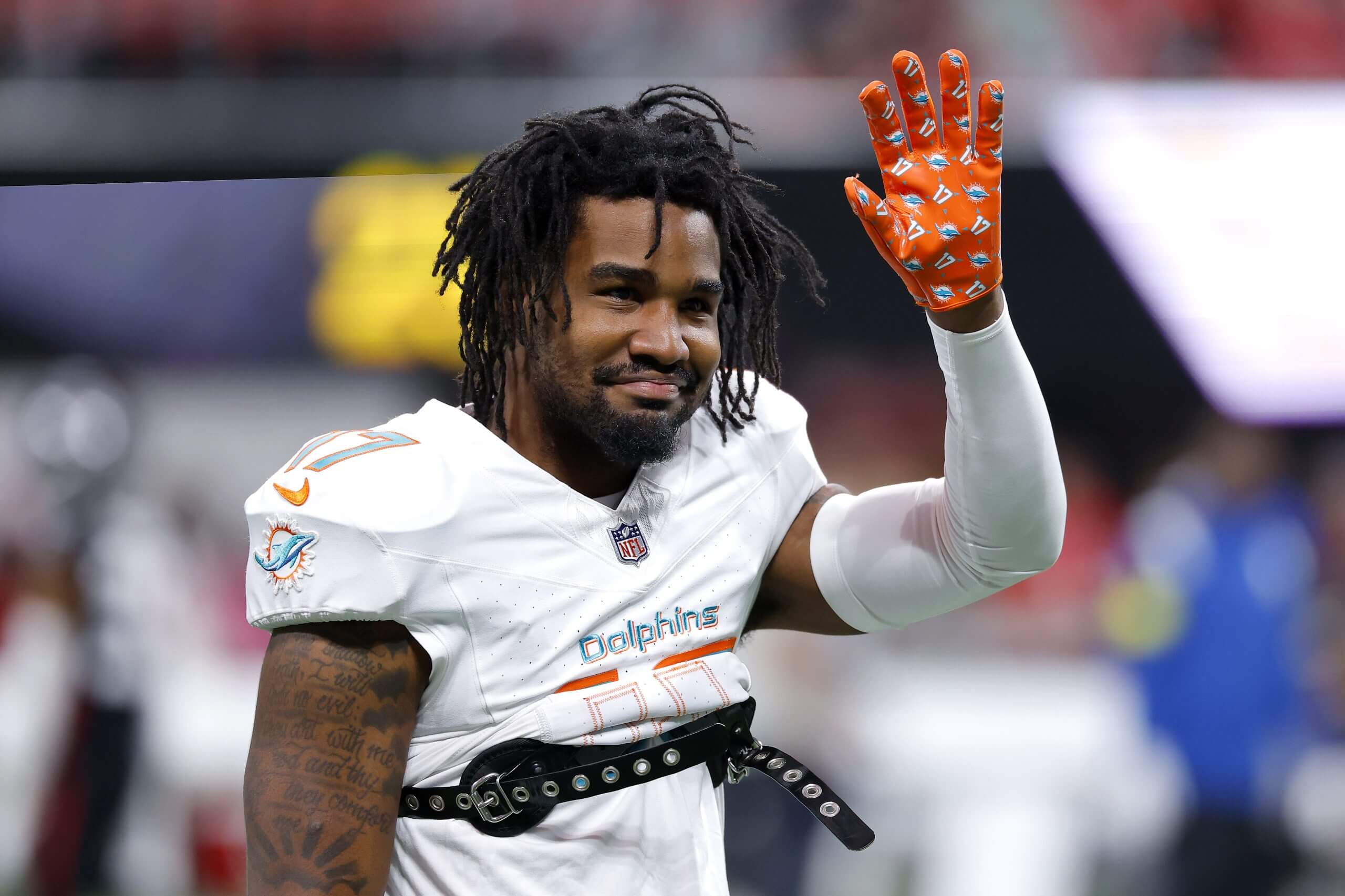 Jaylen Waddle, wearing a white No. 17 uniform with no helmet, waves with his left hand in an orange glove.