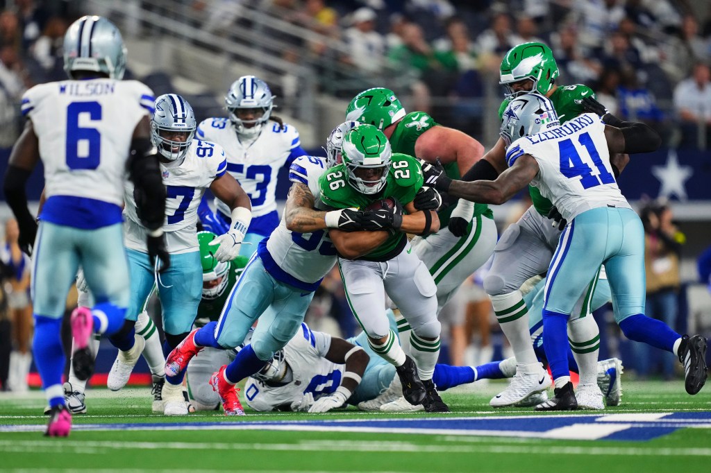 A Philadelphia Eagles player in green uniform carries the ball as he is tackled by multiple Dallas Cowboys players in white and blue uniforms.