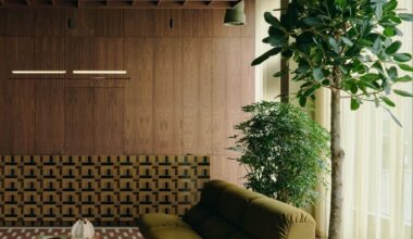 Image of an olive green sofa in a mid-century modern-inspired space with wooden walls and a red rug and lots of plants.