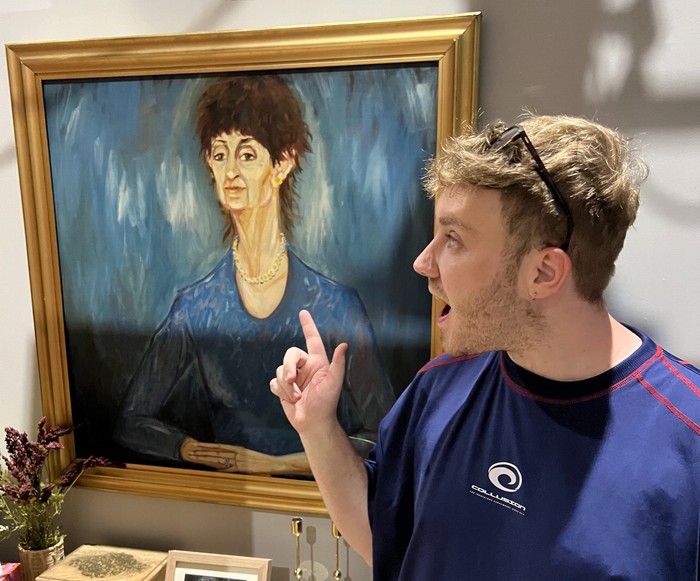 Mrs Mangel painting Radio Times soaps editor Michael Adams, wearing sunglasses and a blue t-shirt, stood beside the blue painting of Mrs Mangel on the set of Neighbours