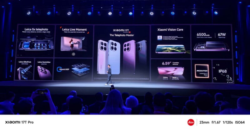 A presenter stands onstage in front of a large screen displaying features and images of the Xiaomi 13T Pro smartphone, highlighting its cameras, battery, display, and other specifications to an audience.