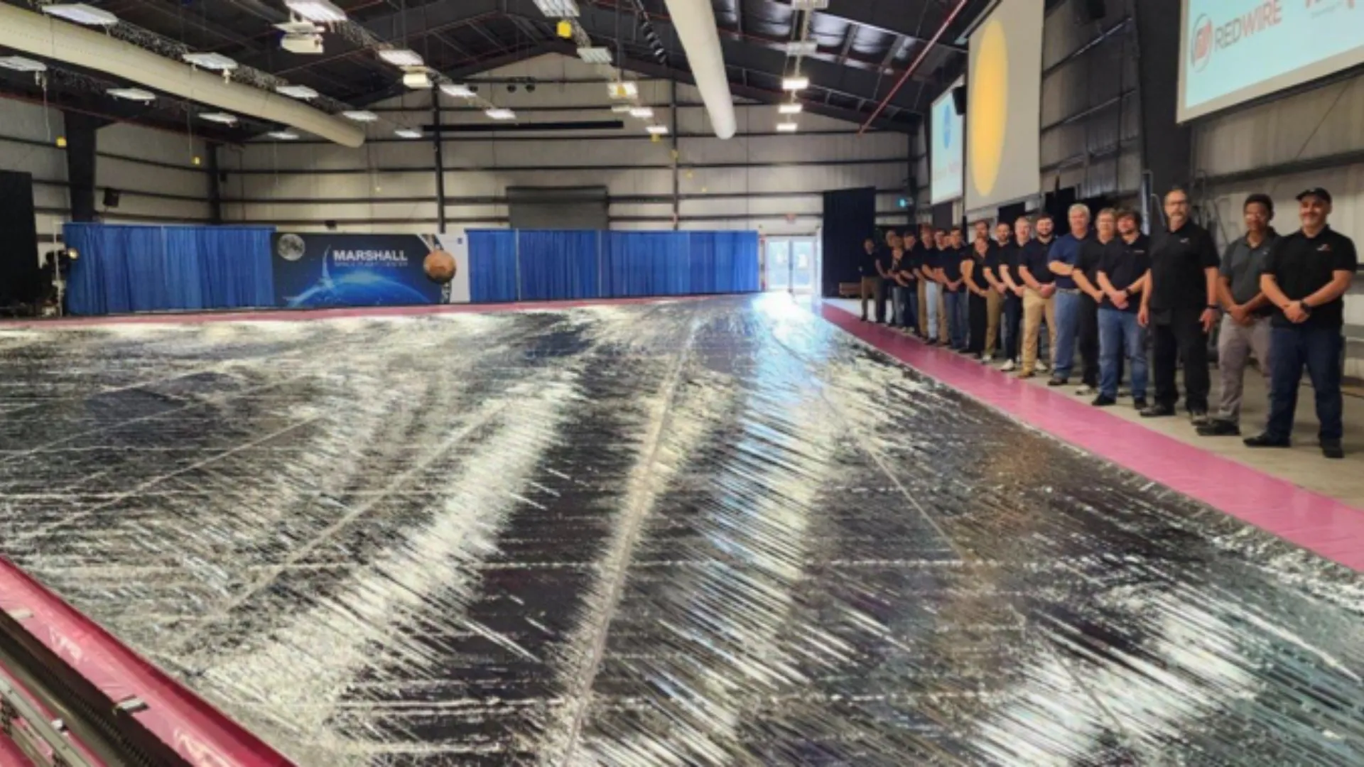 People standing to the side of a huge silvery sail on the ground.