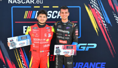 Two race drivers in red and black suits pose with awards on a NASCAR Europe backdrop, each holding a certificate or plaque.