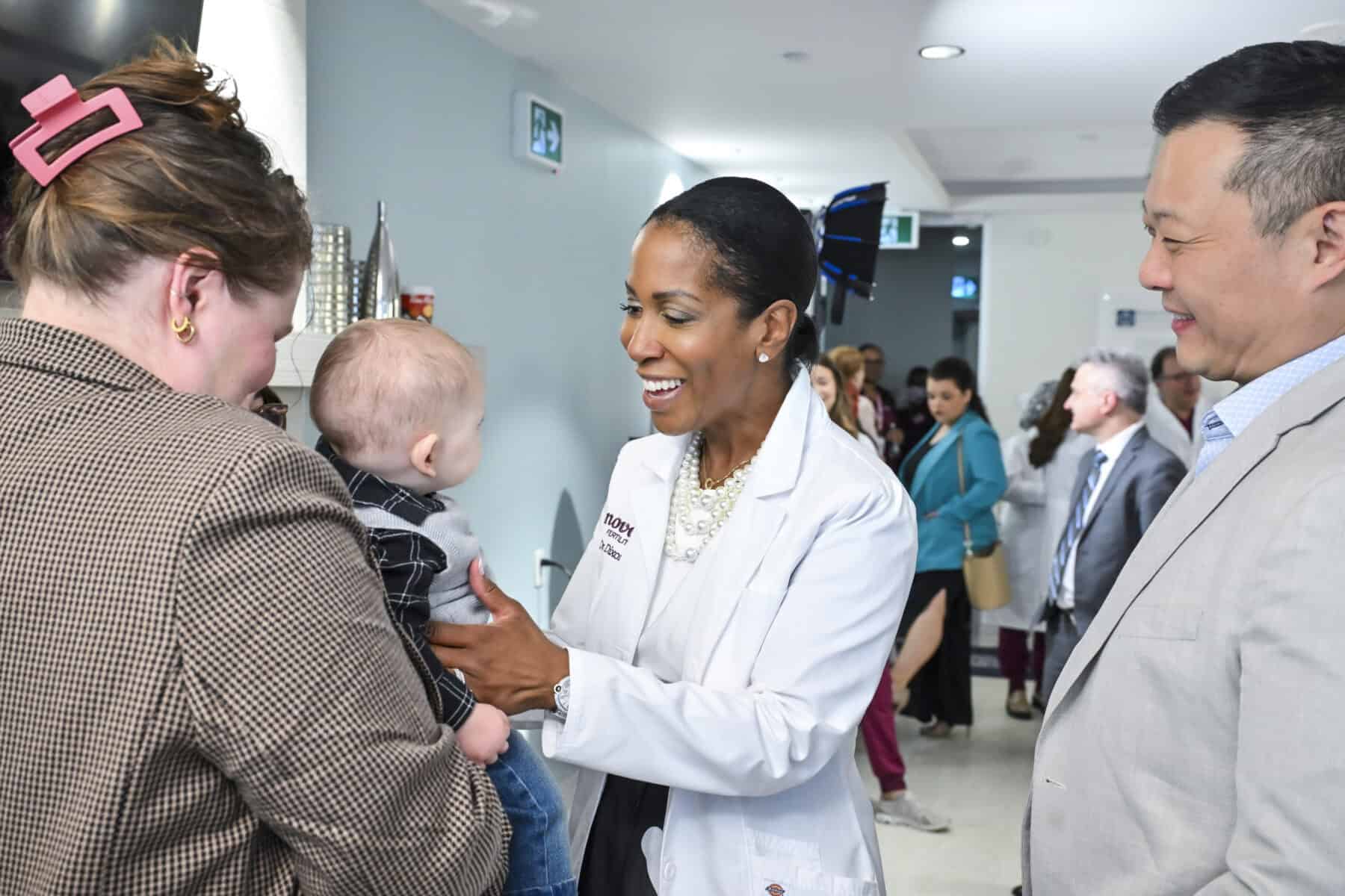 A healthcare professional smiling and talking to a mother holding her baby at a health event in Toronto, showcasing community health services.