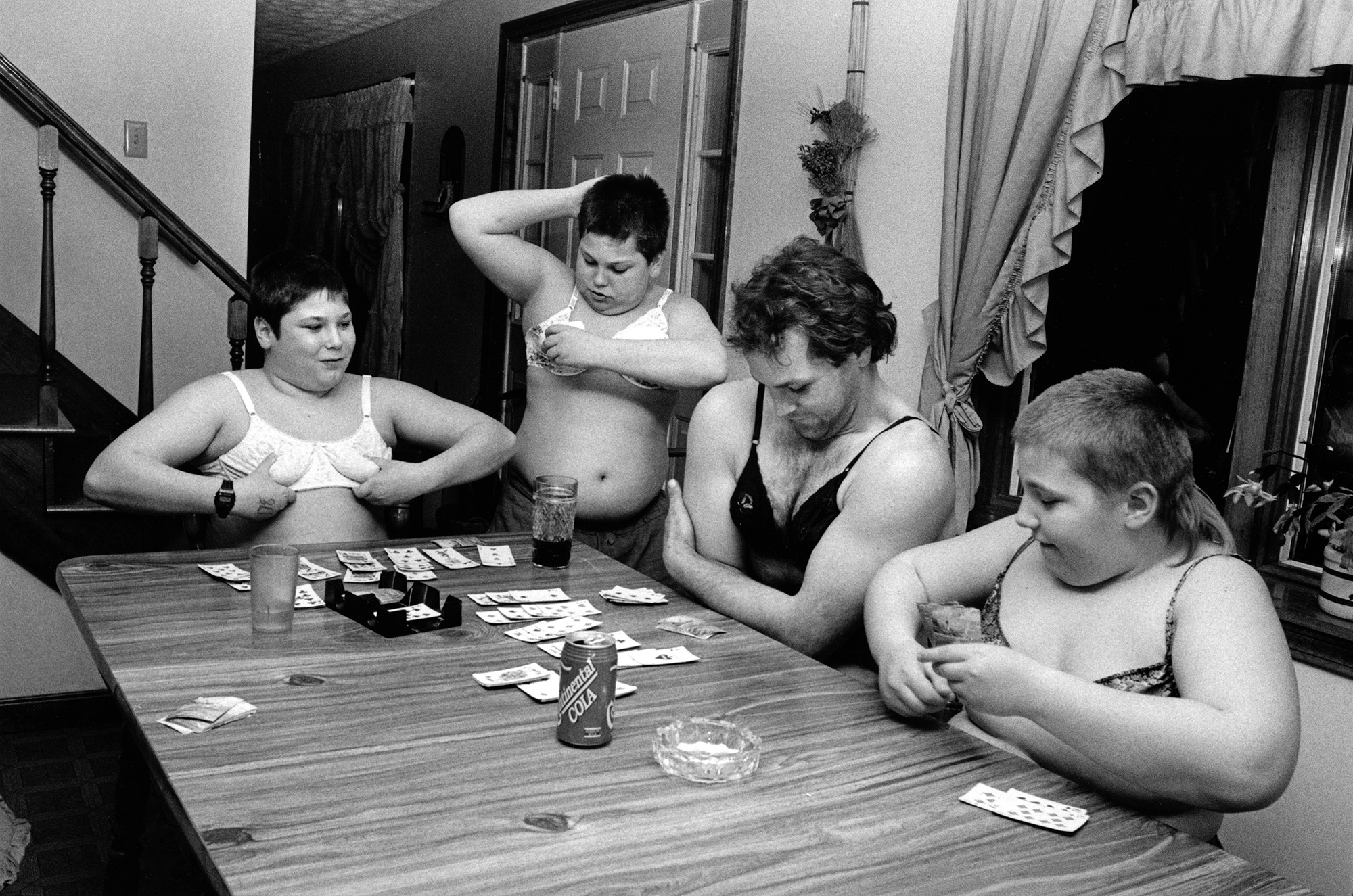 Young boys wearing bras playing cards at a table.