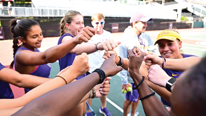 Group of diverse young athletes in a circle joining their fists for a team cheer on a track field.