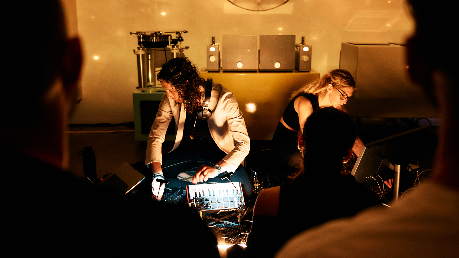 two dj's twirl knobs on electronic devices in front of swirling colored projects on art gallery walls behind them