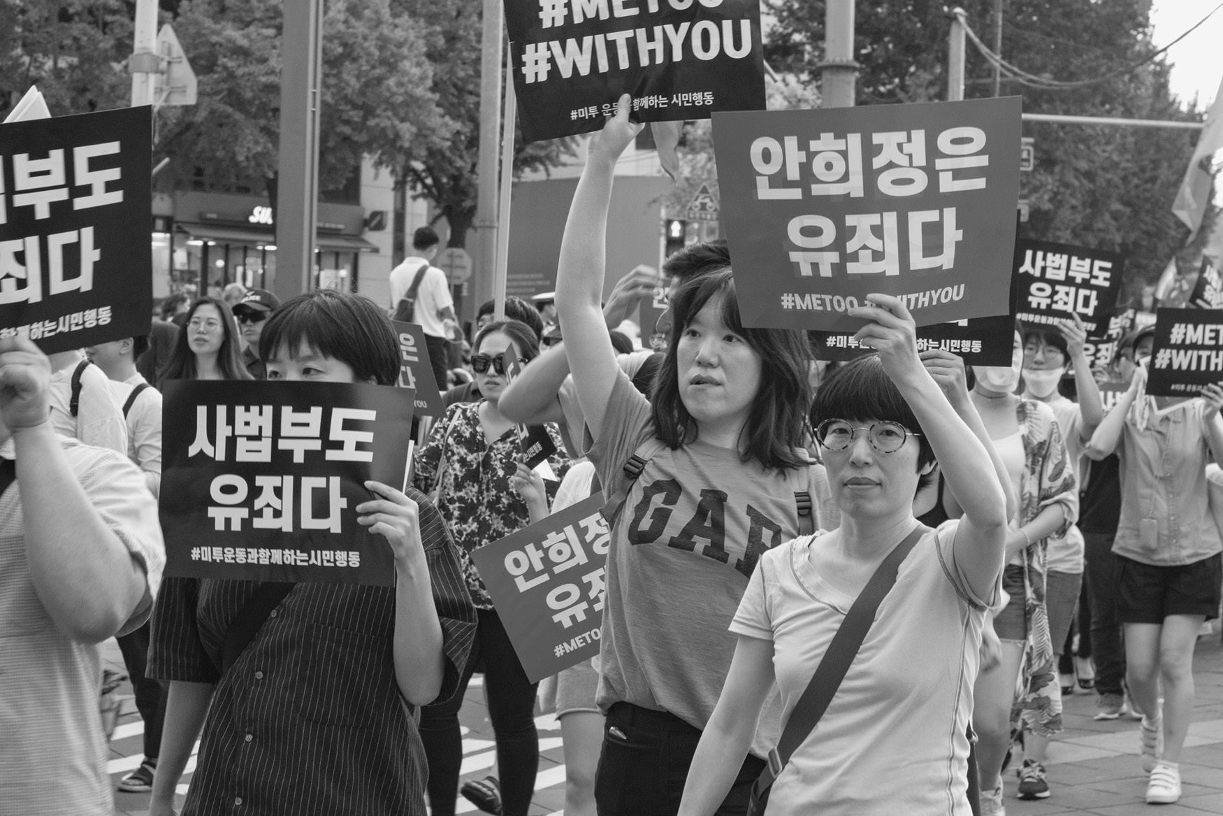 Black and white photo of a protest with people holding signs in Korean and hashtags #METOO and #WITHYOU