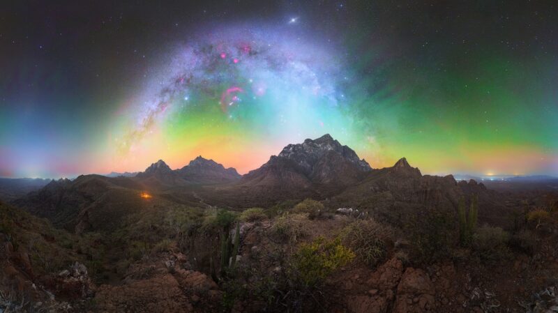 Rocky and mountainous landscape with the Milky Way and rainbow-hued airglow.