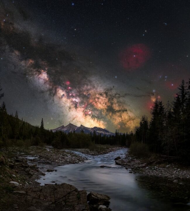 Rugged mountains with snowcaps and a river plus the Milky Way behind.