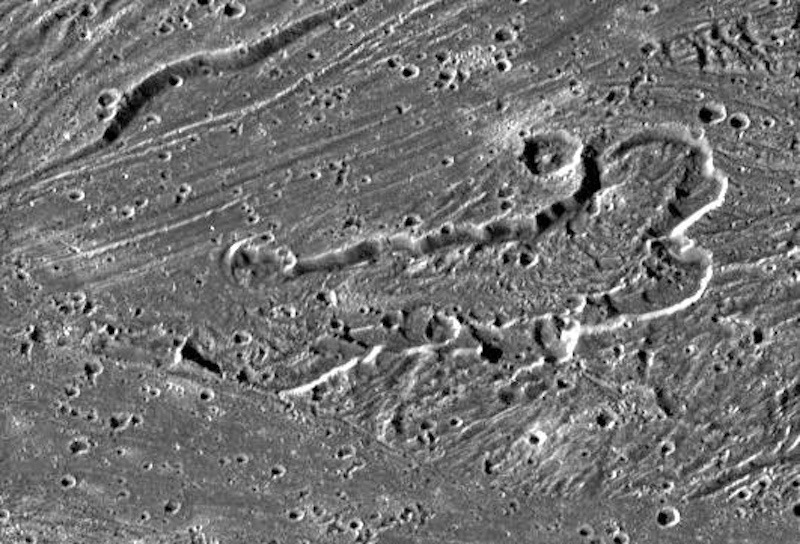 Gray landscape seen from above, with an oblong depression, craters and linear grooves.