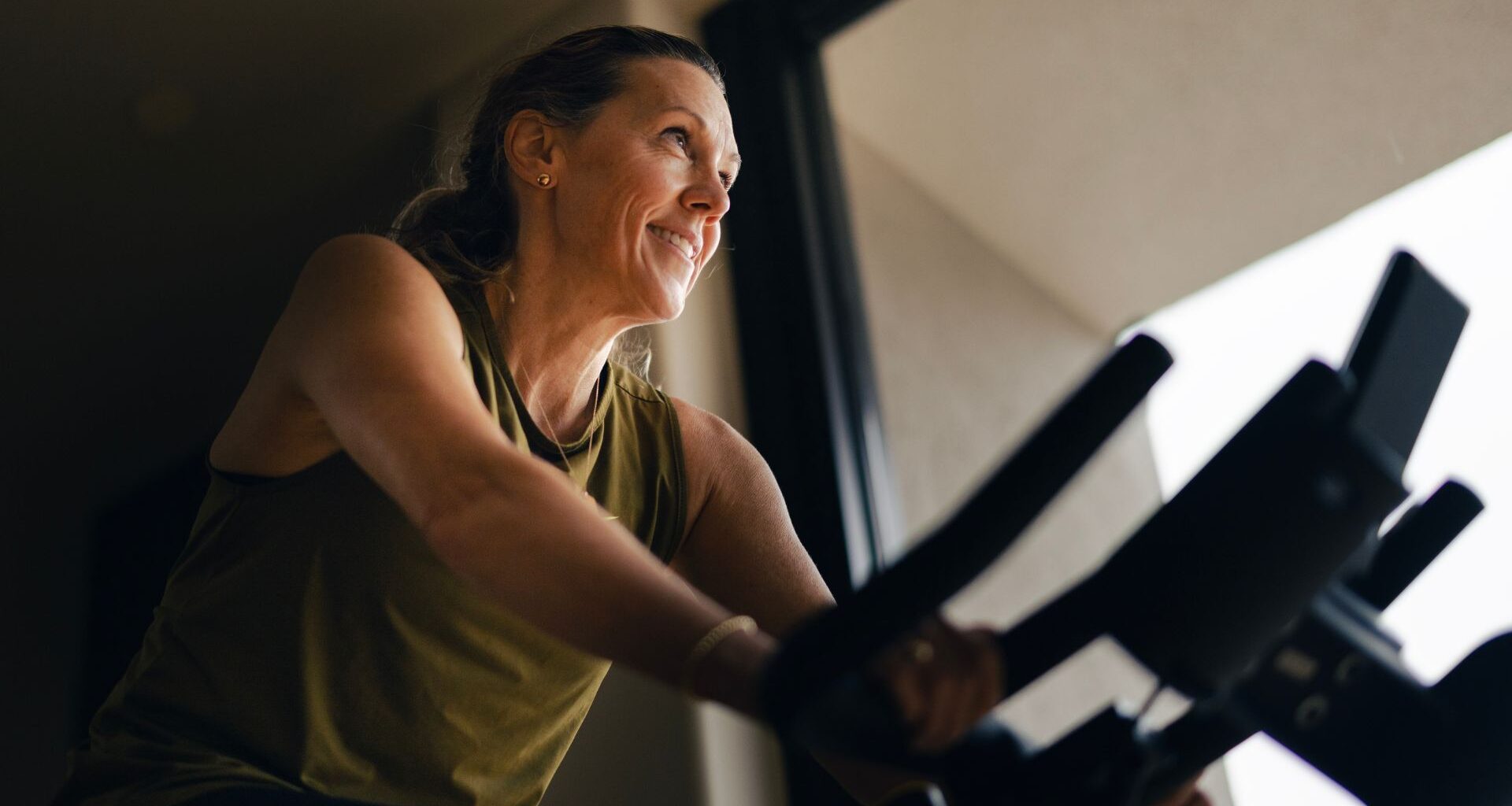 Woman doing 10-minute cycling workout on bike at home, smiling