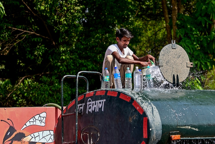 A man fills water bottles from the top of a water tanker. (Photo: PTI)